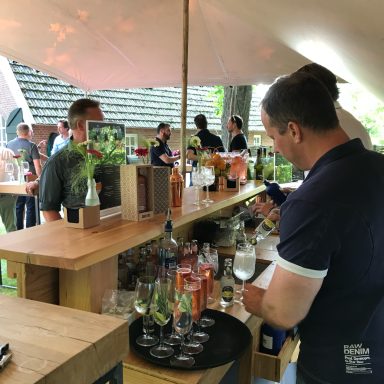 Barman schenkt drankjes in een buitenbar, met gasten op de achtergrond.